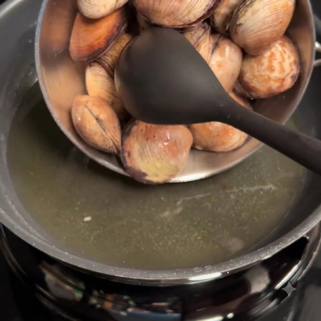 Cleaned clams being poured from a bowl into a pan with garlic oil.