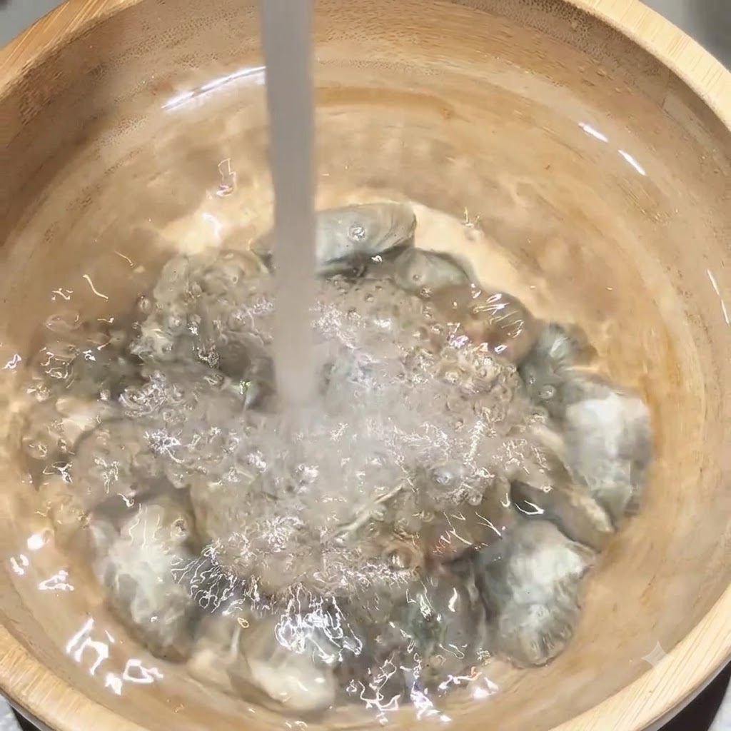 Fresh water pouring directly onto a batch of clams inside a wooden bowl.