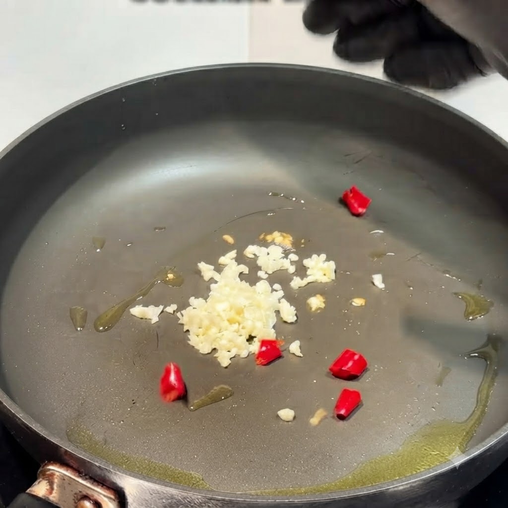Minced garlic and chopped red chili peppers scattered across an oiled pan.