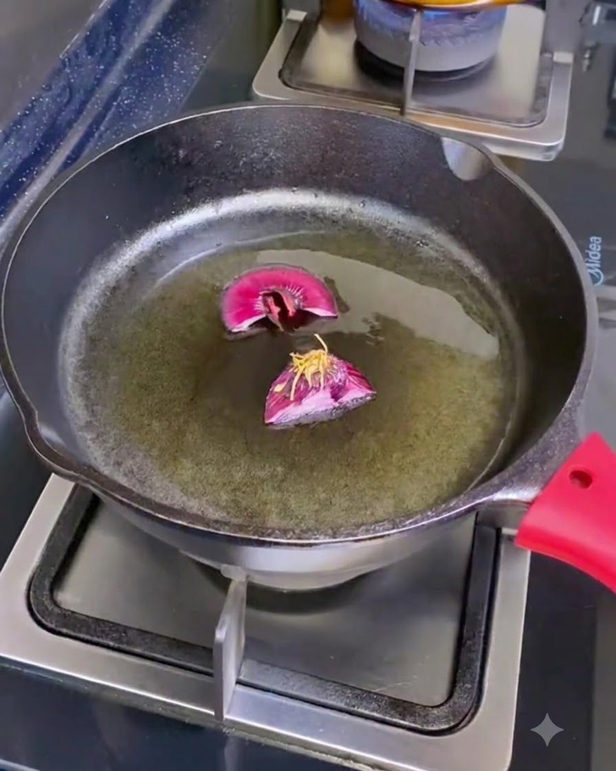 A cast iron skillet on a burner containing olive oil and two cut pieces of shallot roots.
