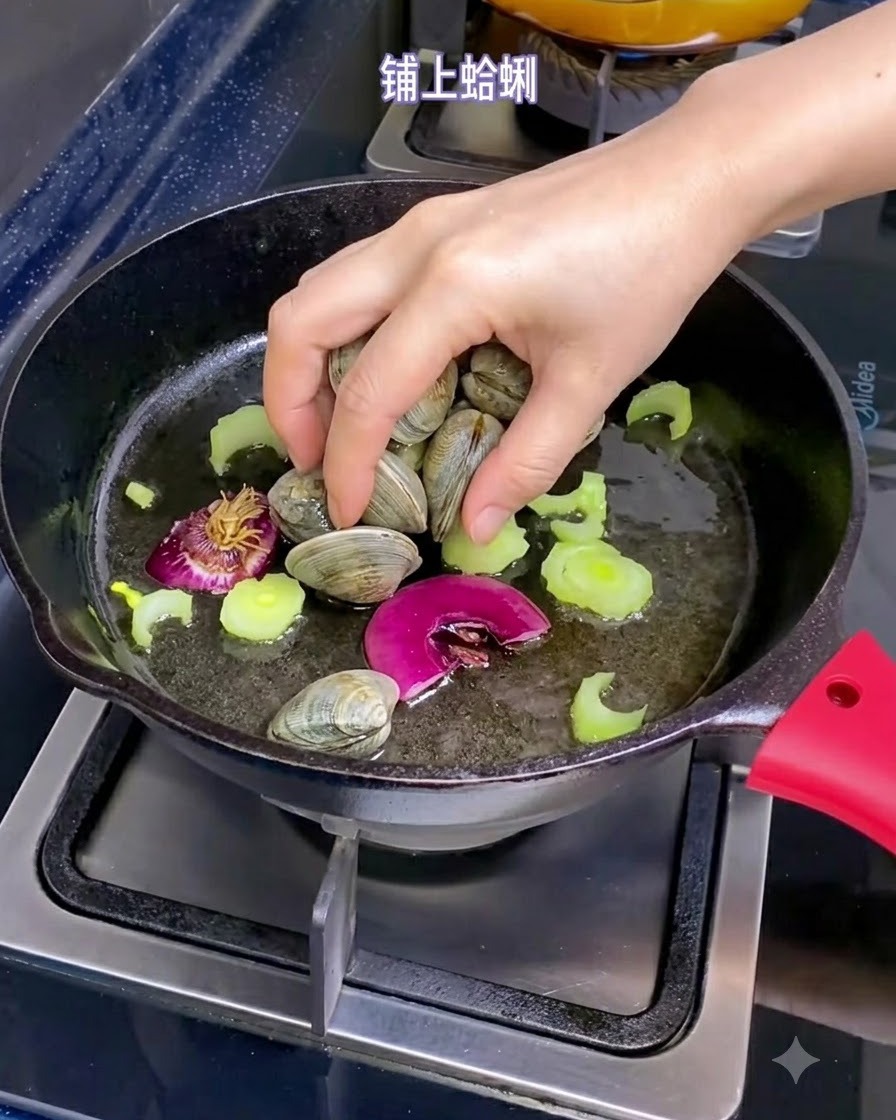 A hand placing fresh clams into a skillet filled with olive oil, shallot pieces, and sliced celery.