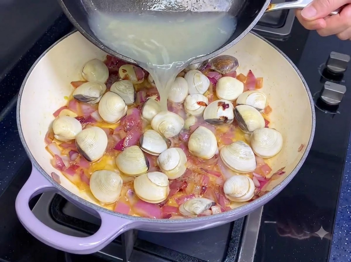 Clam broth being poured from a skillet into a pan with onions and garlic.