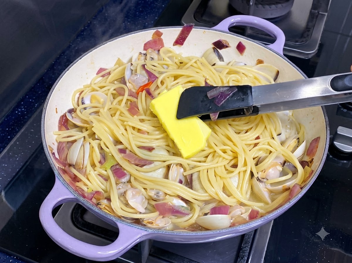 A knob of yellow butter melting into a pan of mixed spaghetti and clams.