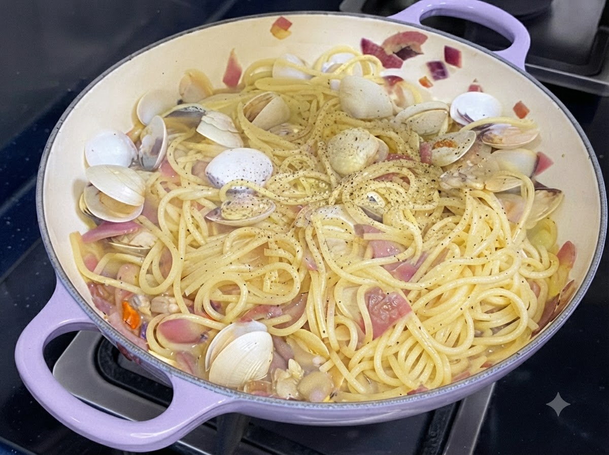 Fresh black pepper being sprinkled over a pan of cooked spaghetti and clams.