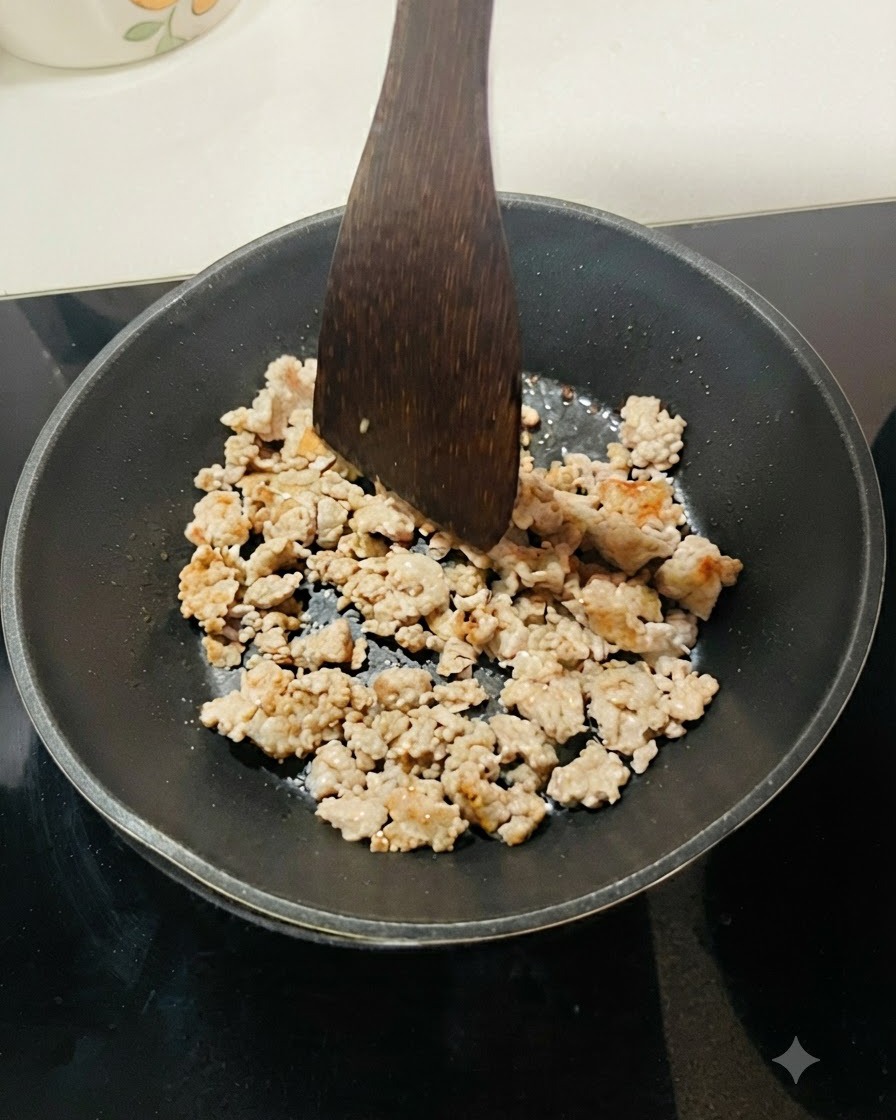 Minced meat being fried in a black pan, separated into small pieces with a wooden spatula.