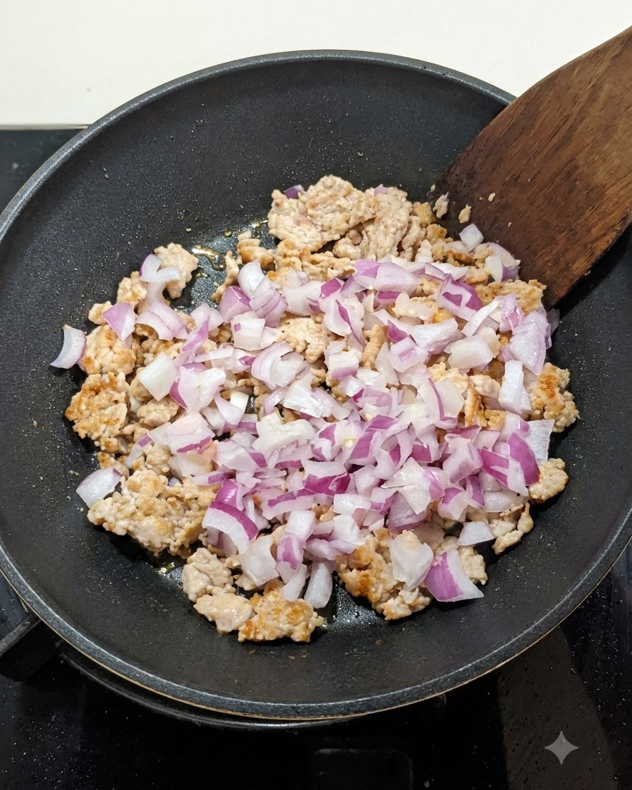 Diced red onions mixed into browned minced meat in a pan, being stirred with a wooden spatula.