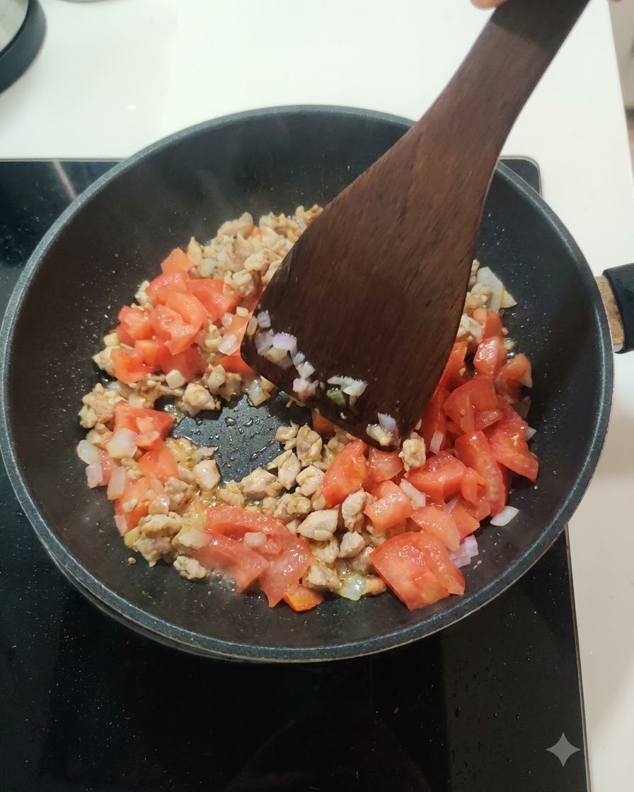 Fresh diced tomatoes being stirred into the meat and onion mixture inside a frying pan.