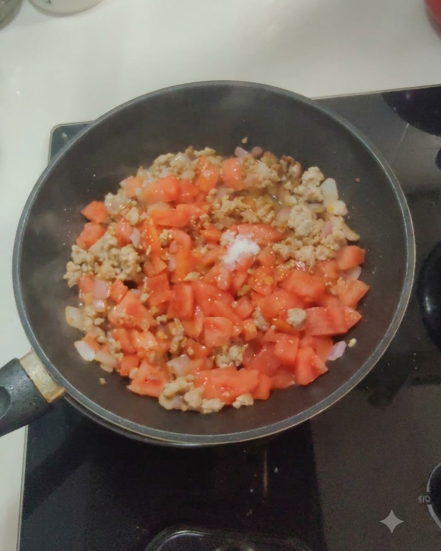 White salt and sugar sprinkled on top of the tomato, onion, and meat mixture in a pan.