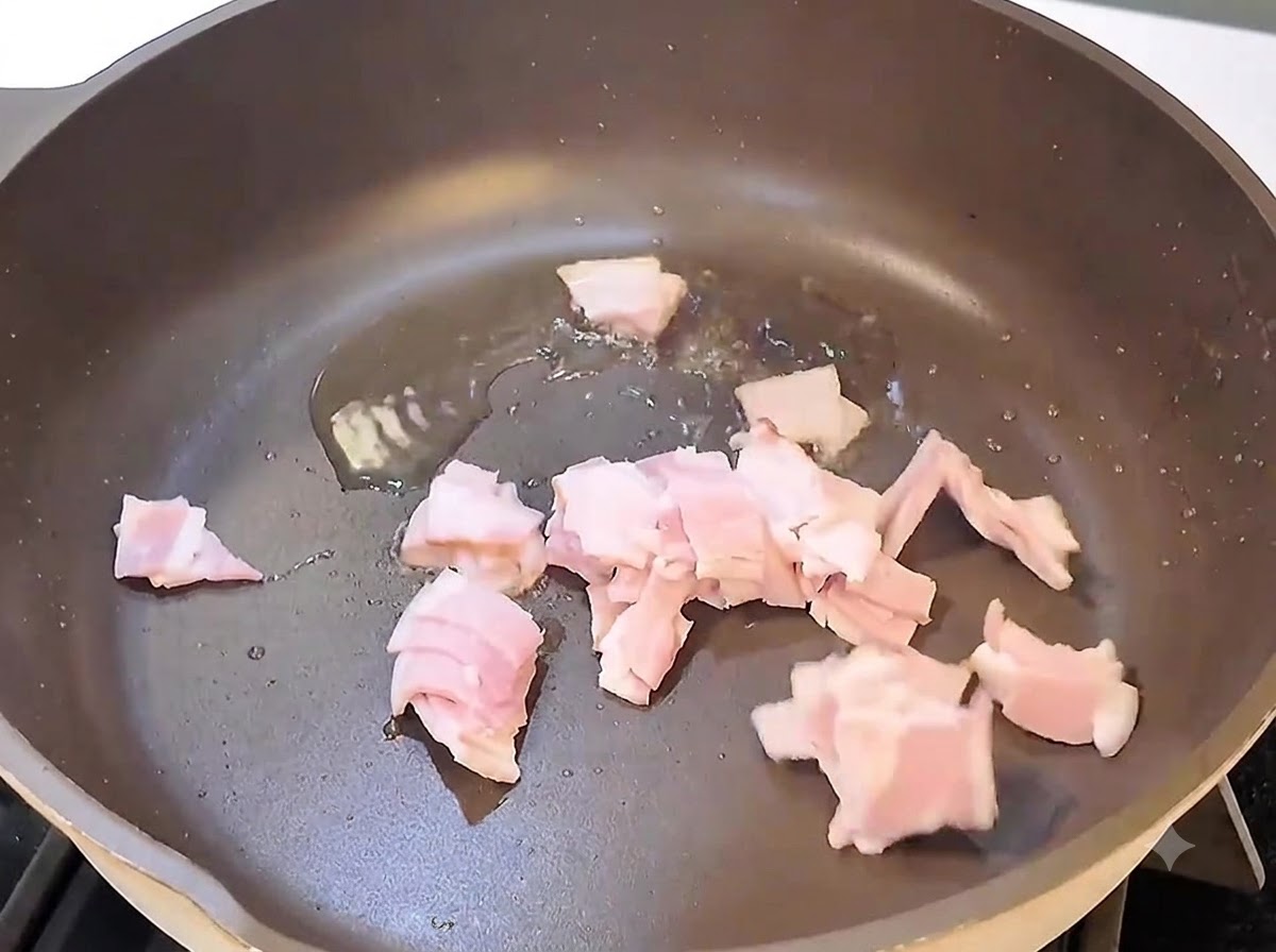Bacon pieces sizzling and frying in a black pan over heat.