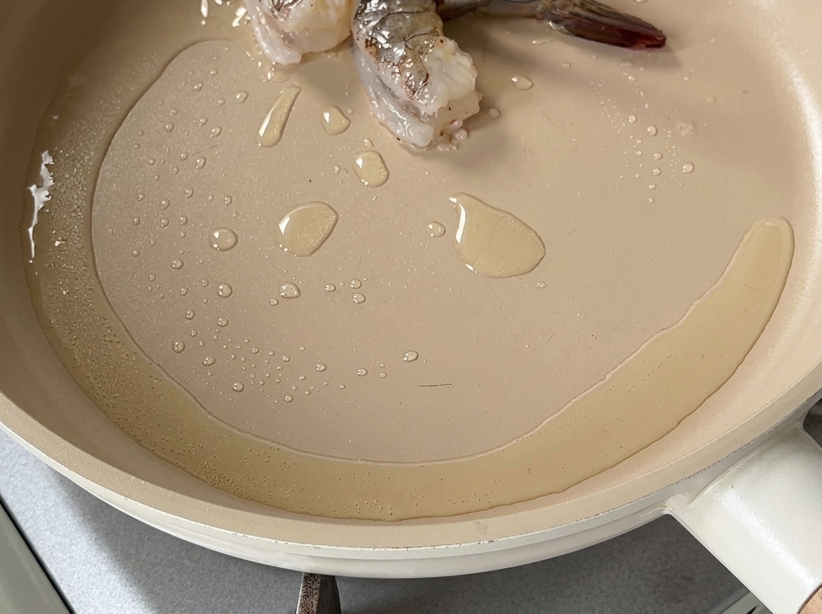 Hot oil shimmering in a shallow pan with a couple of shrimp pieces starting to cook.