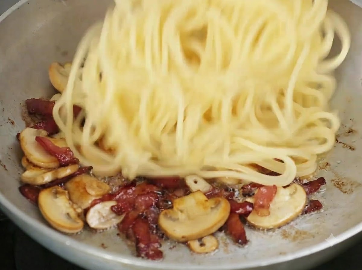Cooked spaghetti being tossed into the frying pan with the cooked ingredients.