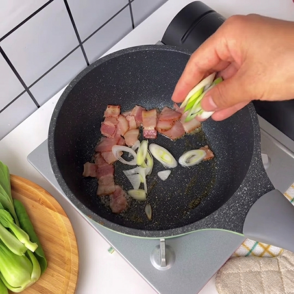 Chopped green onions and chili pepper being sprinkled into a pan with sizzling bacon pieces.