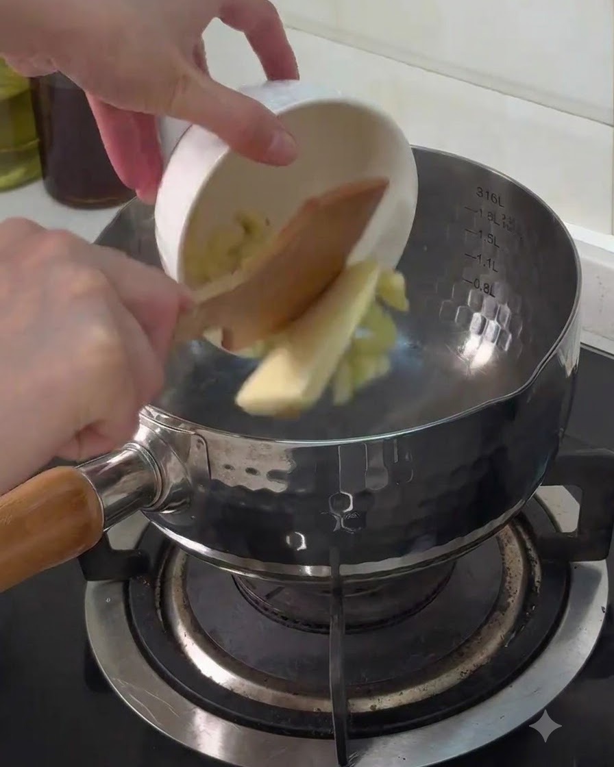 Minced garlic and a piece of butter being poured from a small white bowl into a metal pot on the stove.