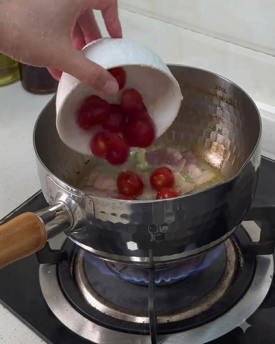 Cherry tomatoes being added from a small white bowl into a pot containing cooking bacon pieces.
