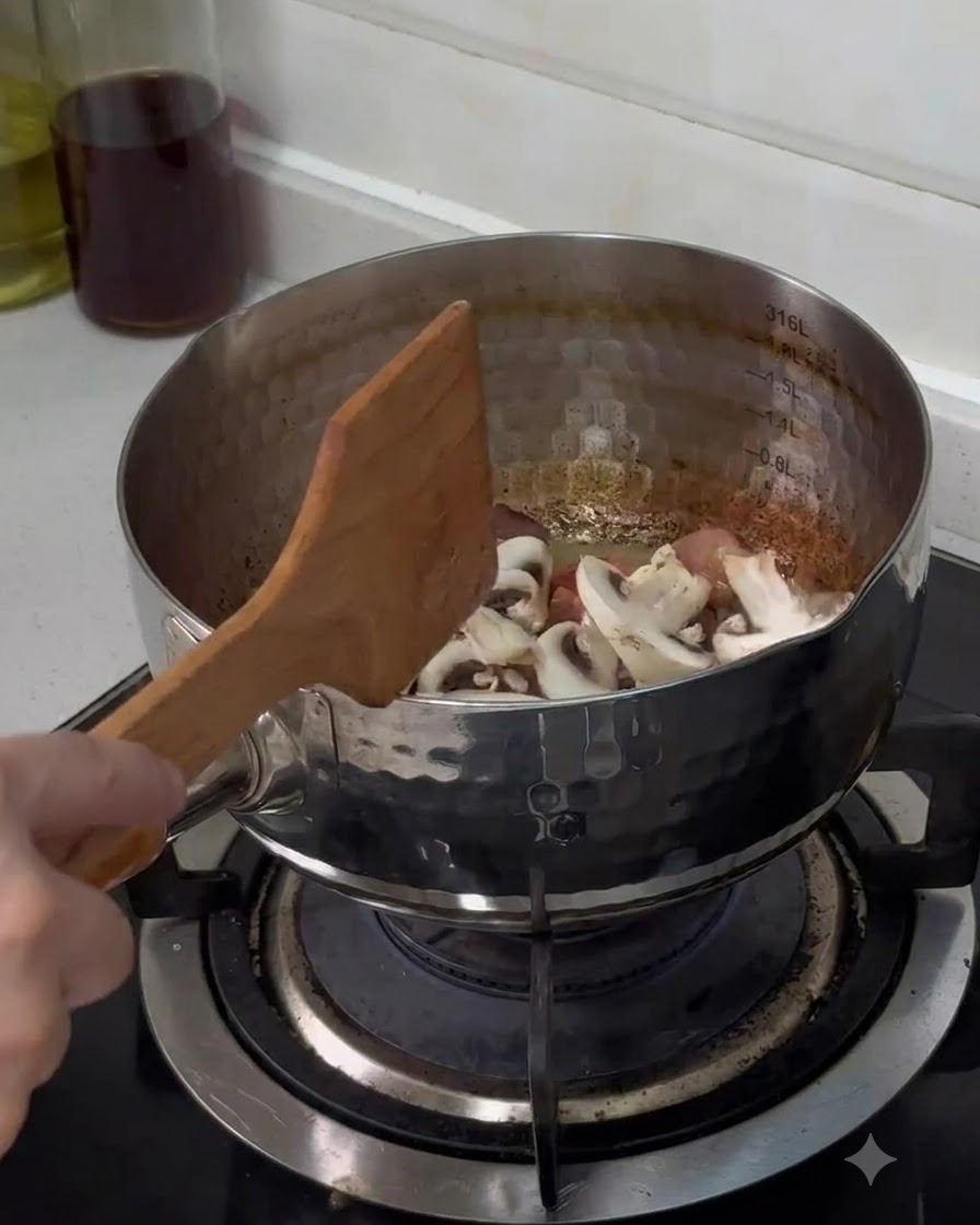Freshly sliced button mushrooms being dropped into the stainless steel pot and stirred with a wooden spatula.