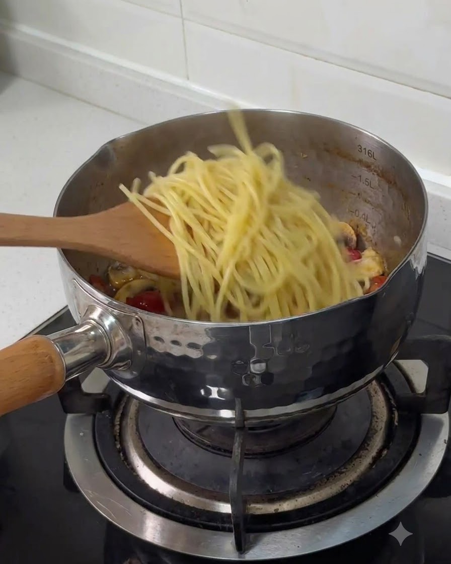Boiled spaghetti being transferred from a wooden spatula into a stainless steel pot with other cooked ingredients.