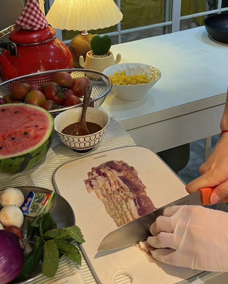 A red onion being sliced in half on a cutting board next to a plate of mushrooms and fresh mint.