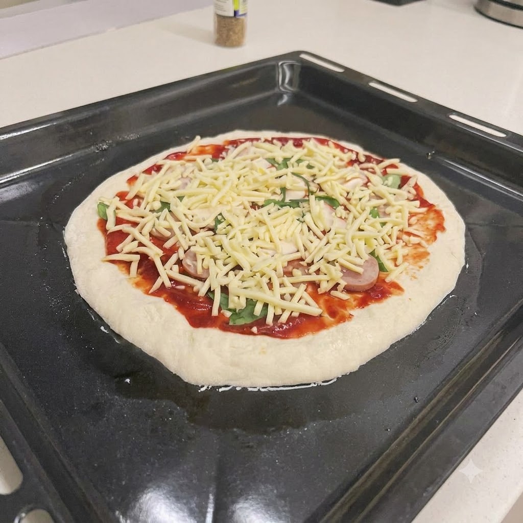 An unbaked pizza topped with red sauce, sausage slices, fresh basil, and shredded cheese on a black baking sheet.