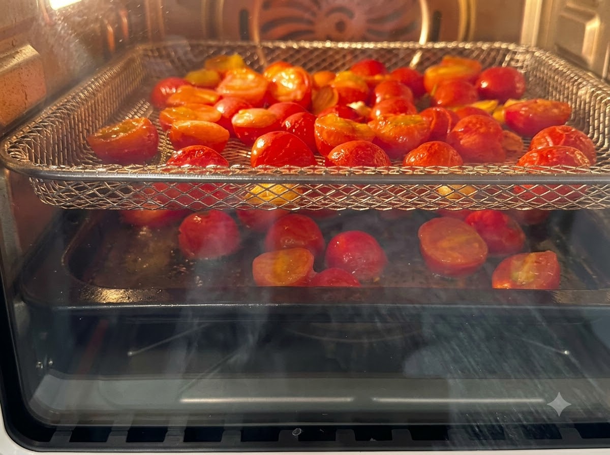 Halved cherry tomatoes arranged on air fryer racks baking inside the appliance.