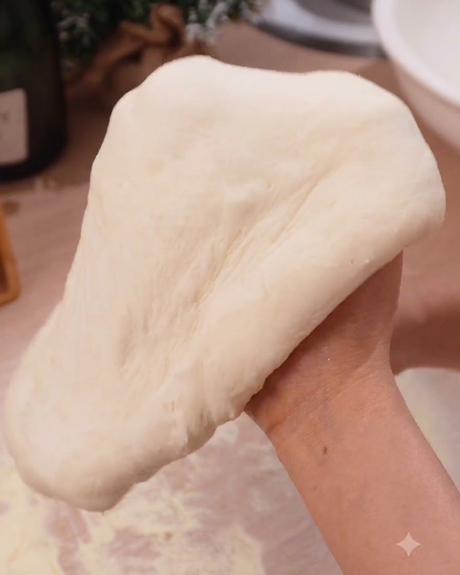 Pizza dough being stretched smoothly over closed hands in a kitchen setting.