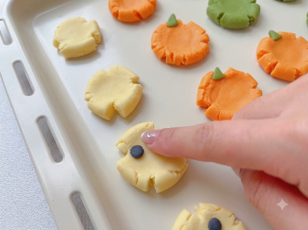 Small colored dough pieces being attached to flattened cookie bases to form spooky designs.