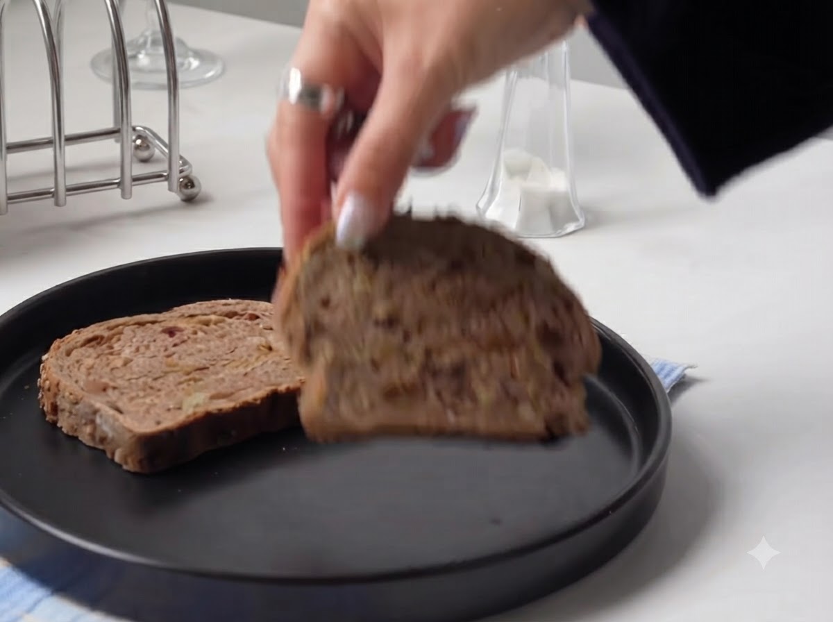 A hand placing a thick slice of rustic bread onto a round black plate.