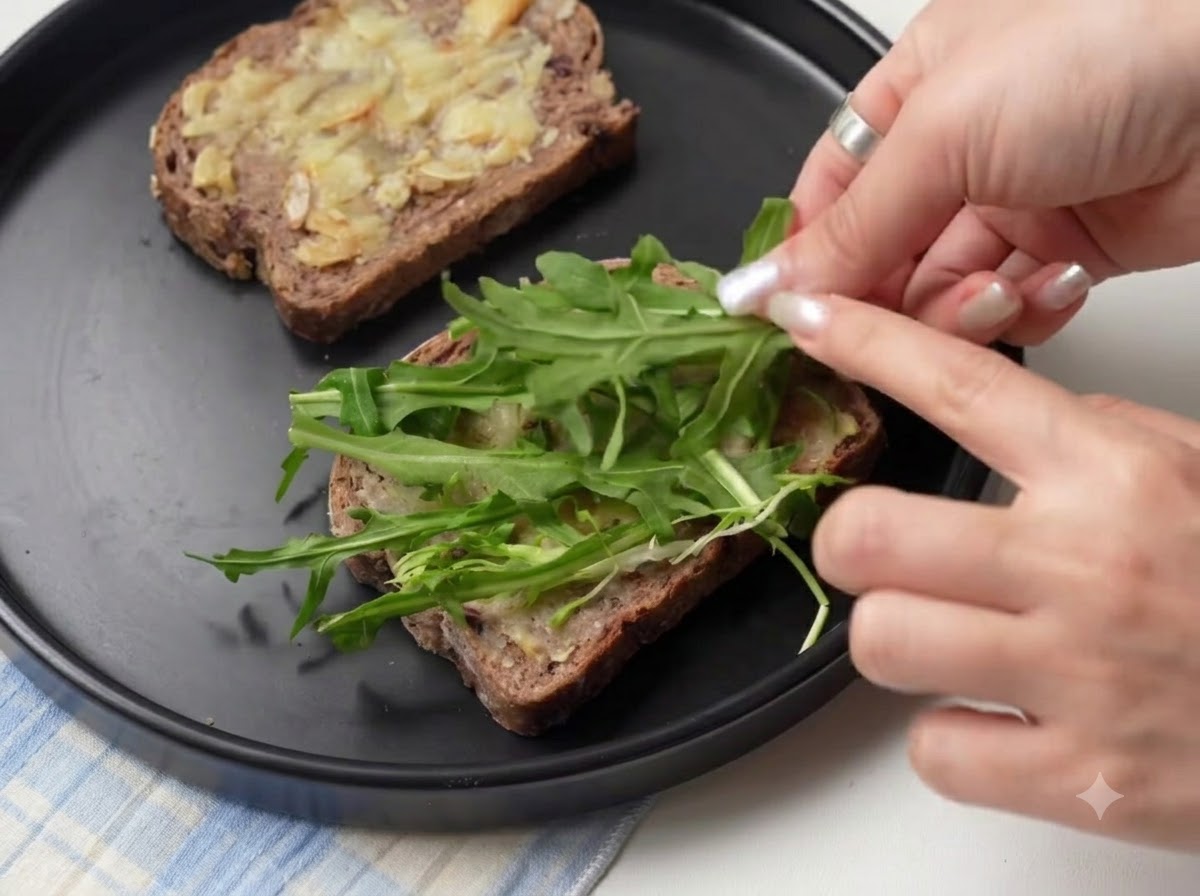 Fresh green arugula leaves being arranged on top of bread slices layered with roasted garlic.