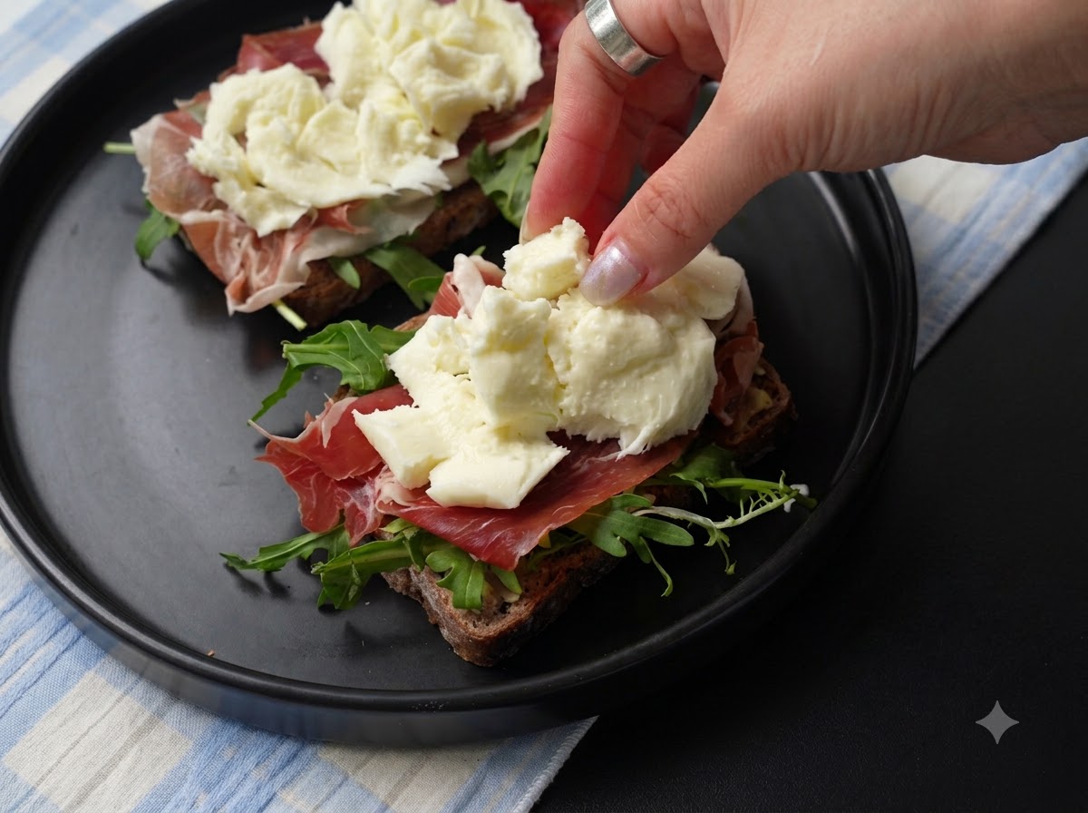 Fresh pieces of torn mozzarella cheese being placed over the ham layer on the sandwich.