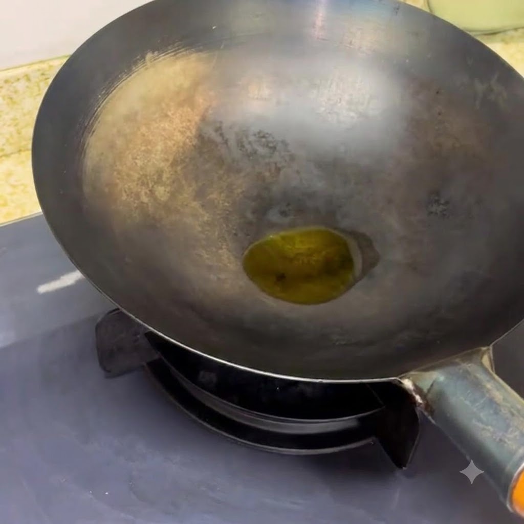 A black wok resting on a stove burner with a small pool of oil heating inside.