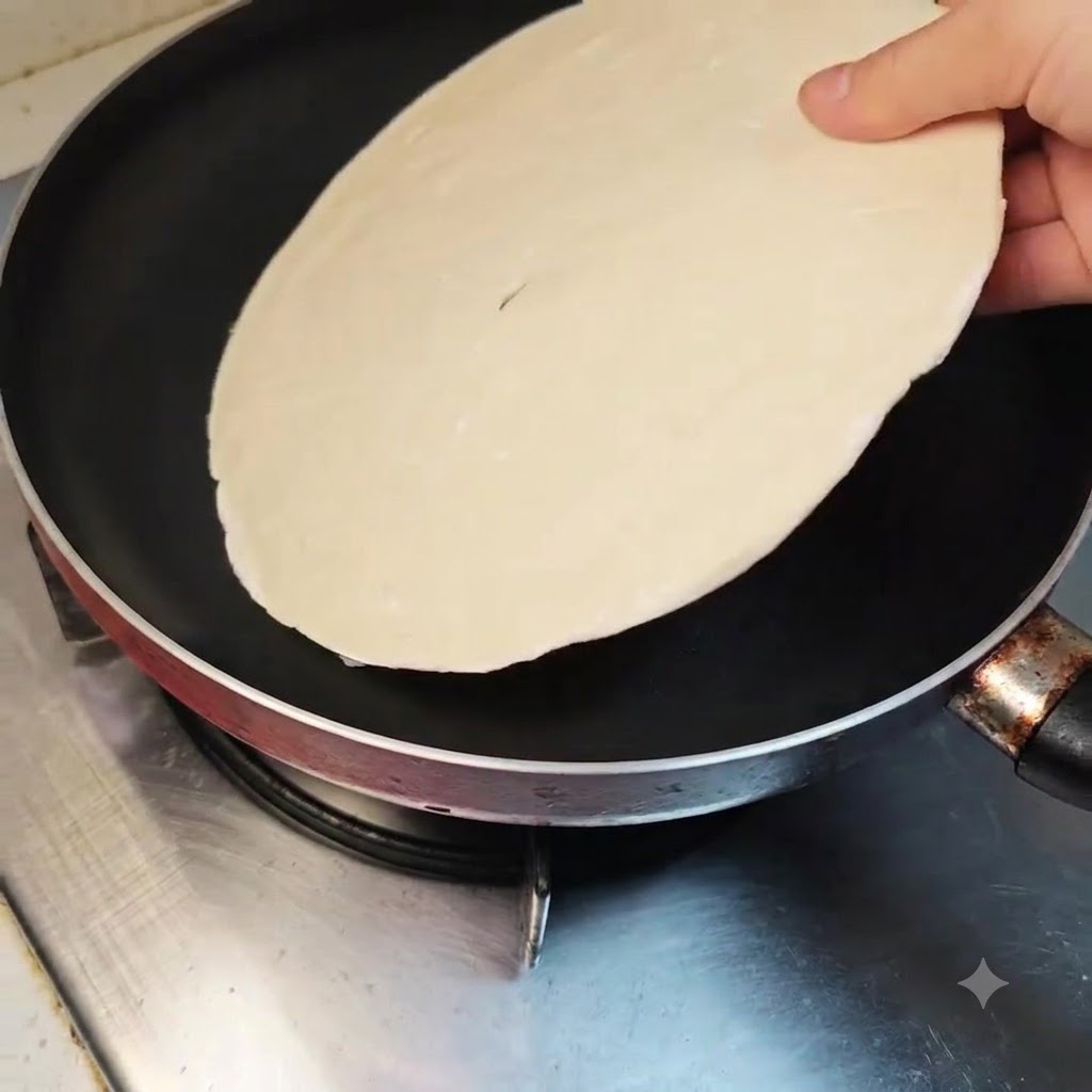 A scallion pancake being laid flat inside a clean non-stick frying pan on an unlit stove.