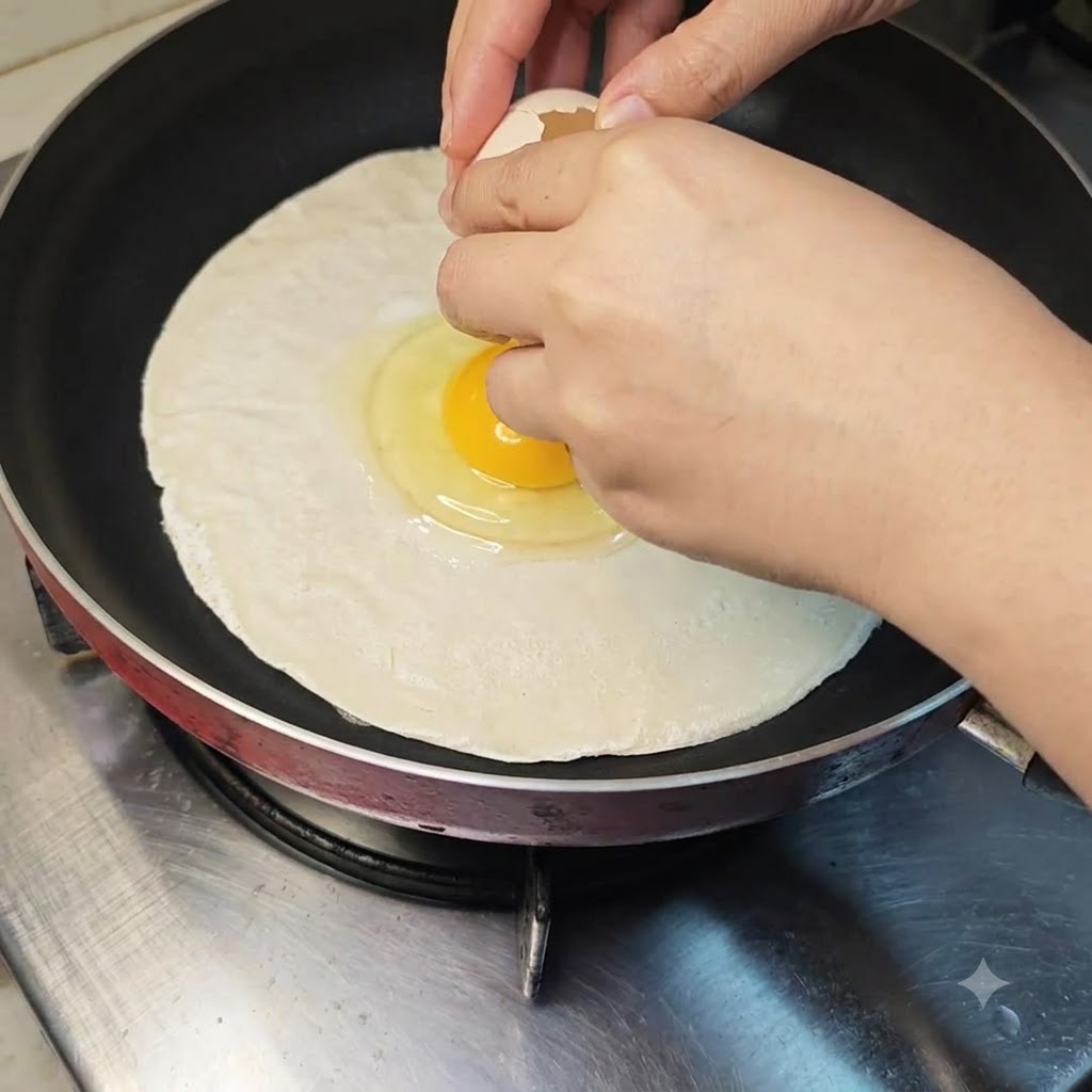 An egg being cracked directly onto the middle of a raw scallion pancake in a frying pan.