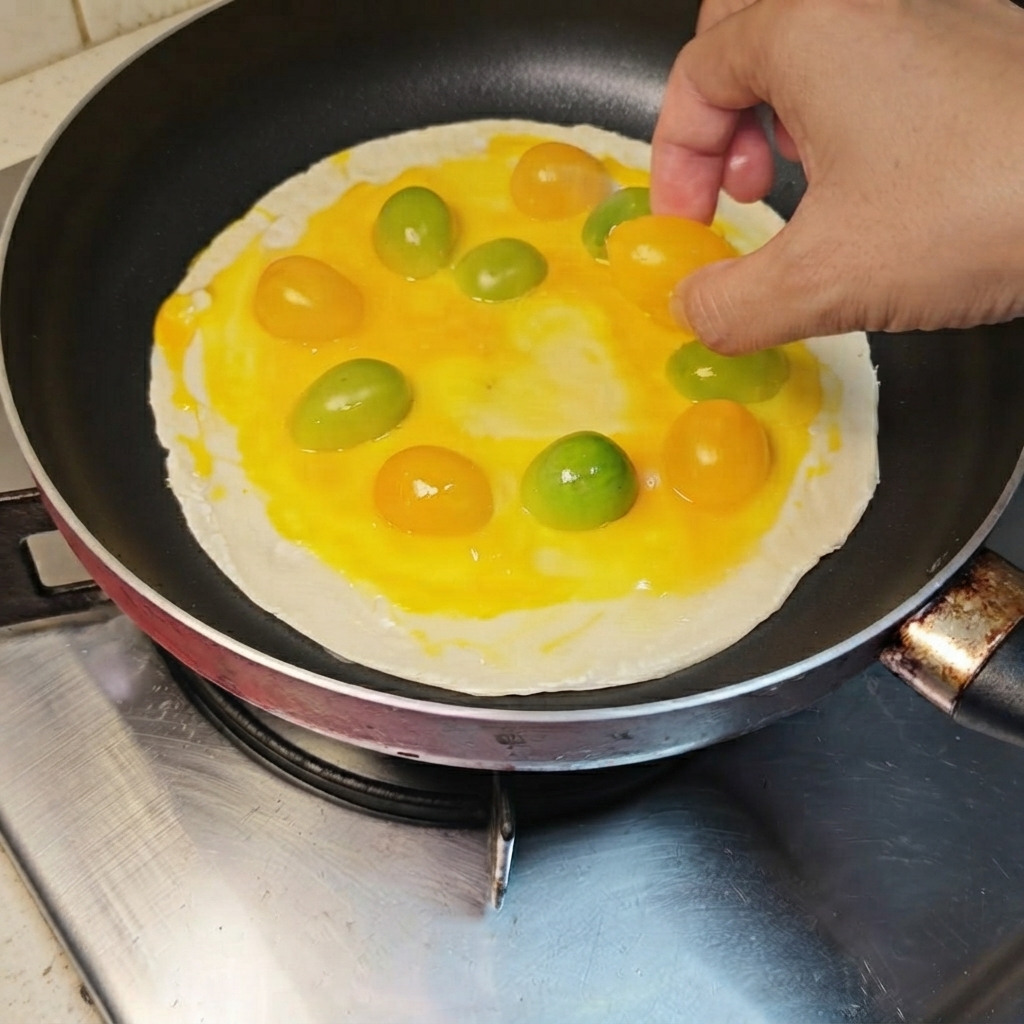 Yellow and orange cherry tomatoes being arranged in a circular pattern over the egg-coated pancake.