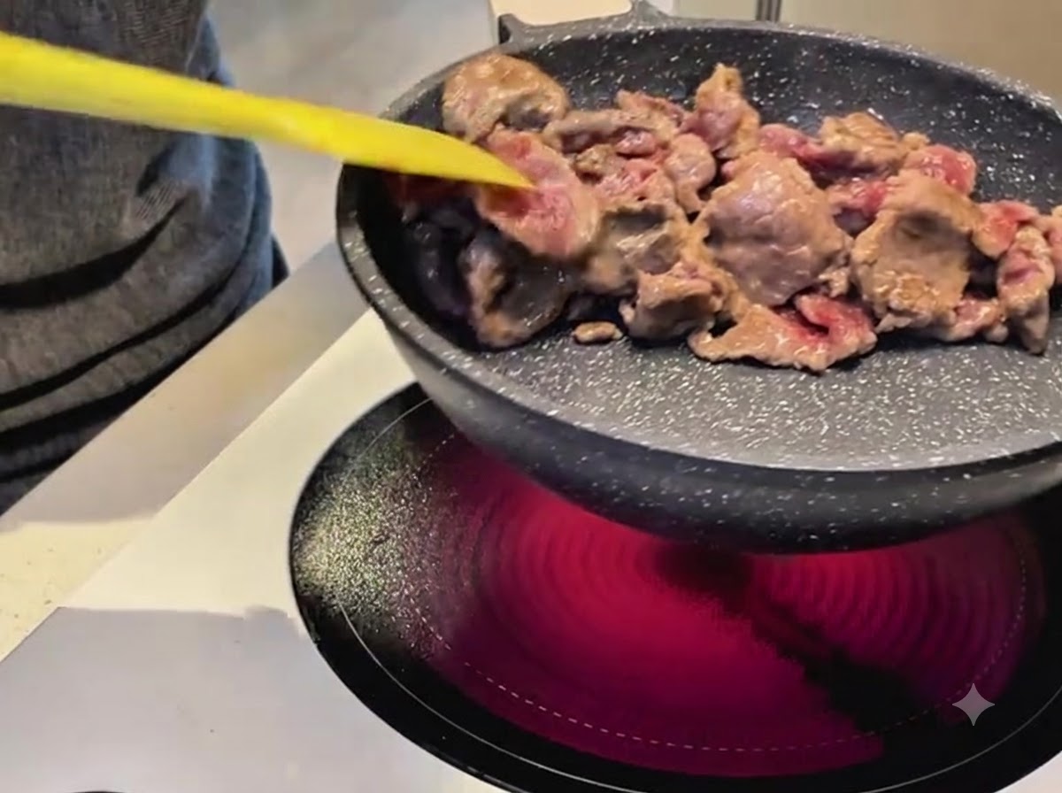 Using a yellow spatula to stir fry beef slices in a non stick pan over an electric stove.