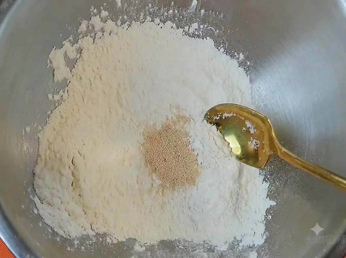 A metal bowl containing flour, a pile of yeast, and a golden spoon resting inside.