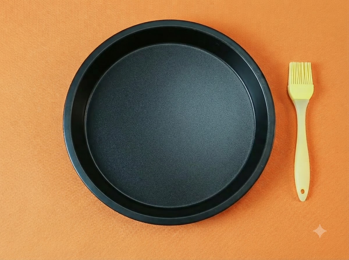 An empty black round pizza pan paired with a yellow silicone oil brush on an orange background.