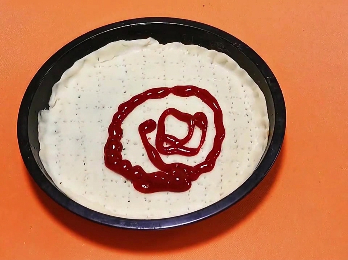 A spiral pattern of bright red tomato sauce being squeezed onto the center of a raw pizza dough base.