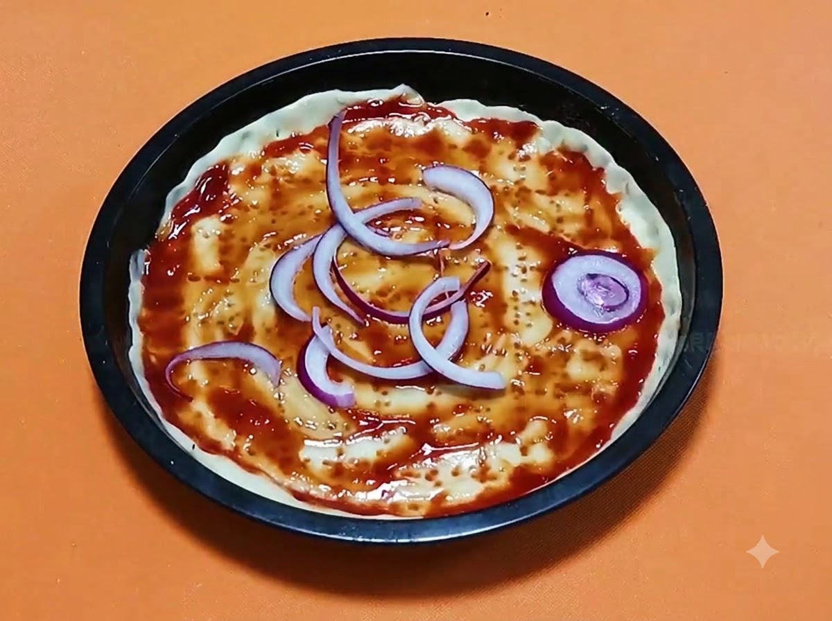 Sliced red onion rings arranged over a tomato-sauced pizza dough base inside a black round baking pan.