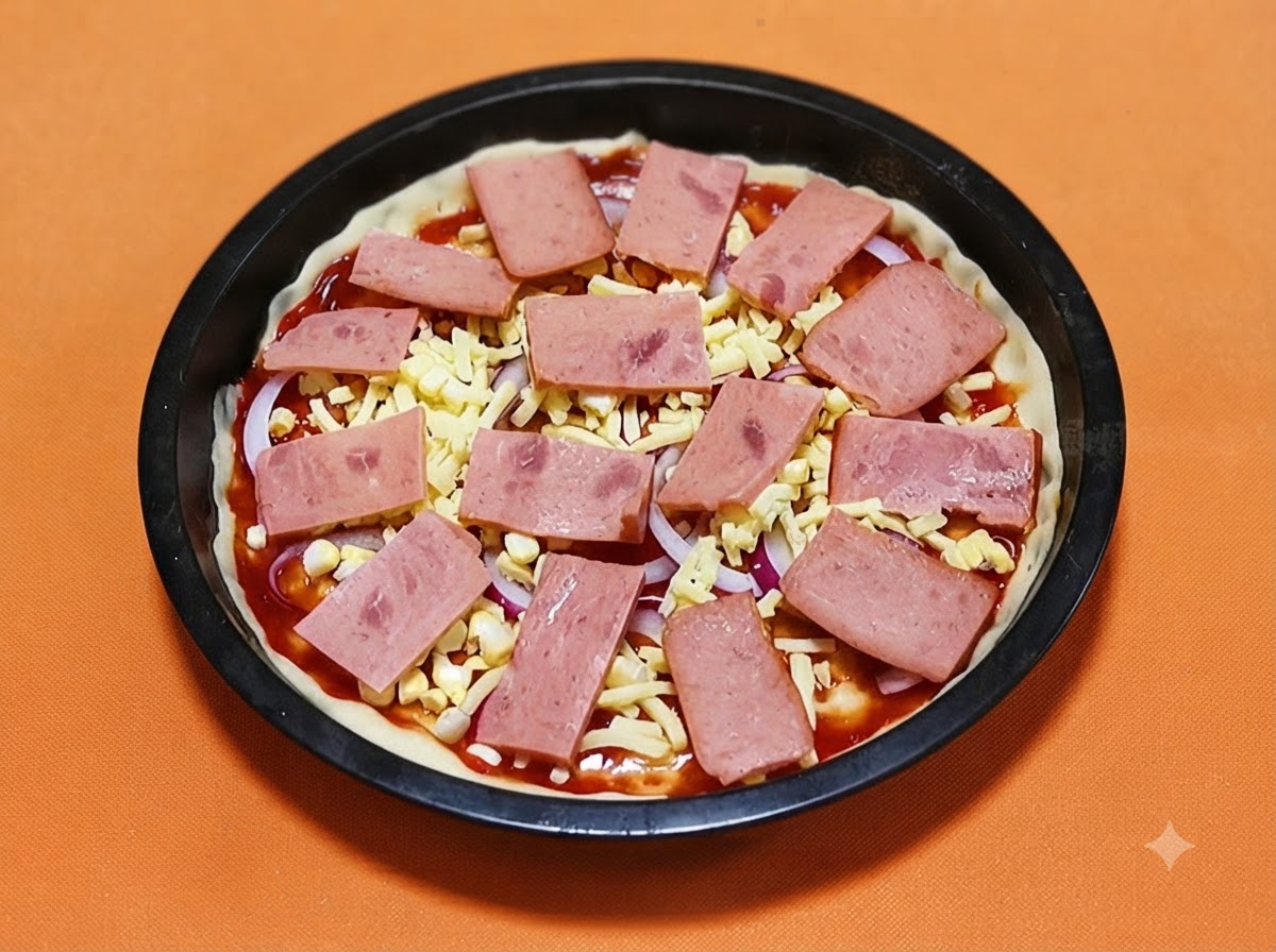 Rectangular slices of pink ham laid out systematically over a pizza crust topped with cheese and onions.