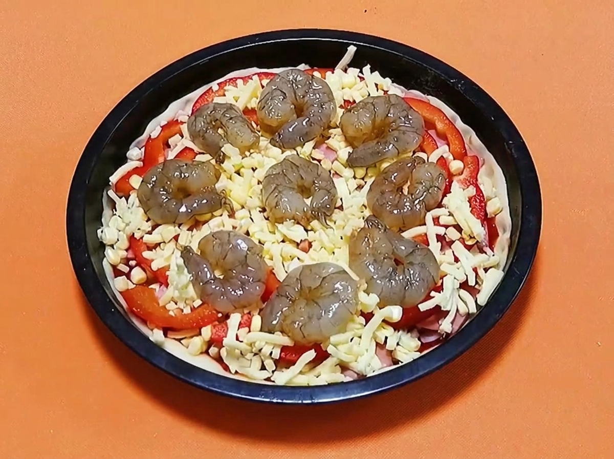 Raw marinated shrimp arranged in a circle on top of a pizza with cheese, peppers, and ham.