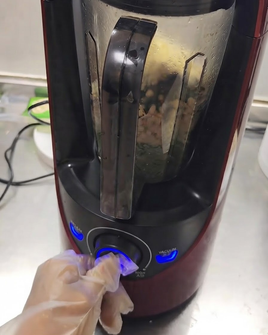 A blender operating with ingredients mixing inside while a hand turns the dial.