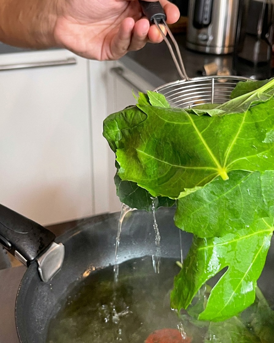A strainer lifting freshly blanched green leaves out of a boiling pot of water.