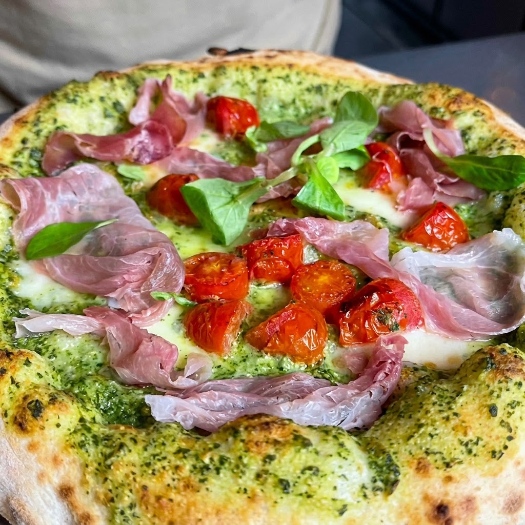 Fresh green herbs and chopped walnuts being sprinkled across the top of a pizza.