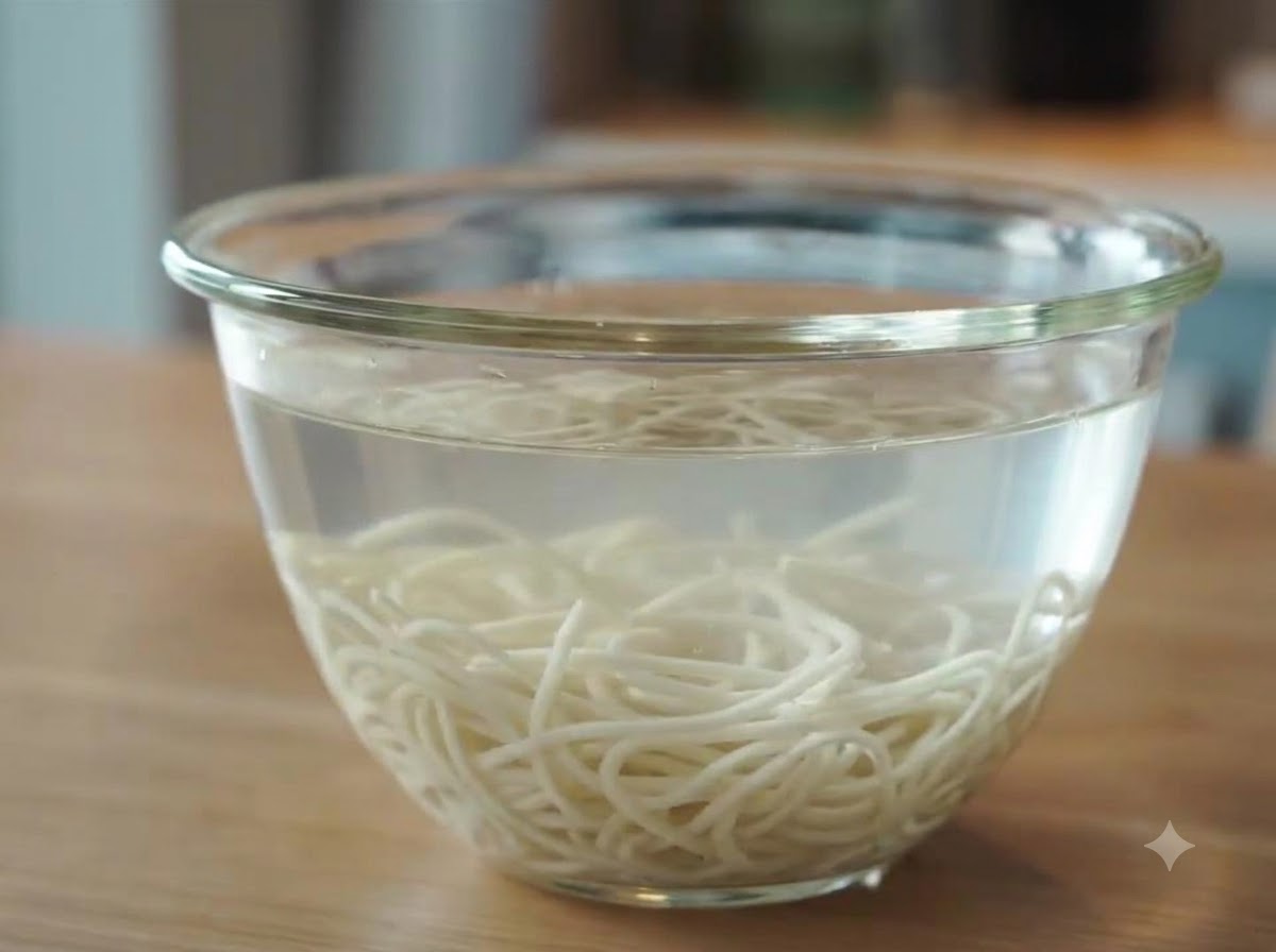 Freshly cooked ramen noodles submerged and cooling in a glass bowl filled with cold water after rinsing.
