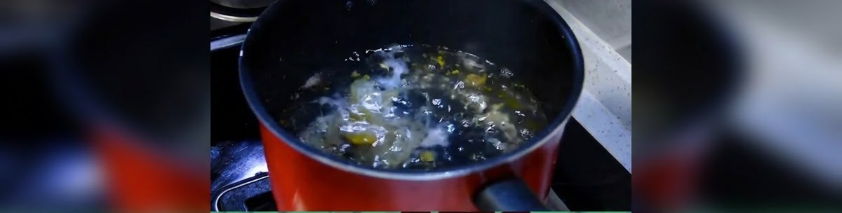 A dark cooking pot with water coming to a bubbling simmer on the stove.