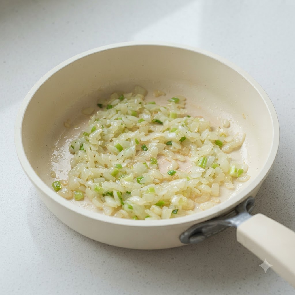 Chopped onions and scallion whites sautéing in a white pan.