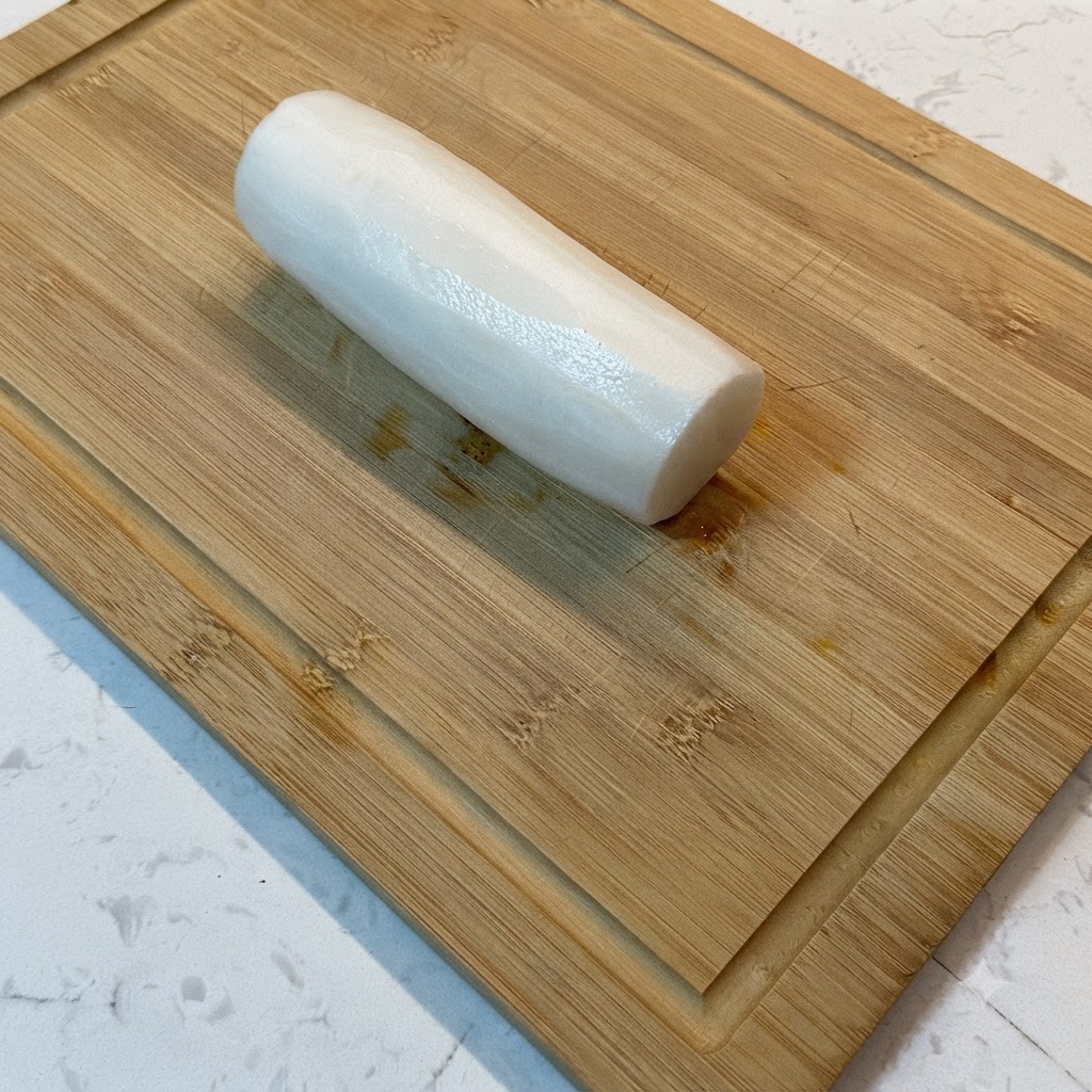 A white radish being cut into thin shreds on a wooden cutting board.