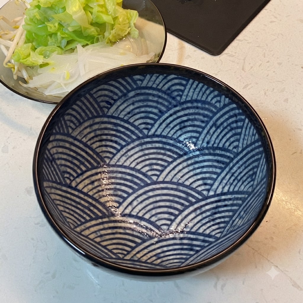 A blue patterned serving bowl placed next to a plate of layered vegetables.