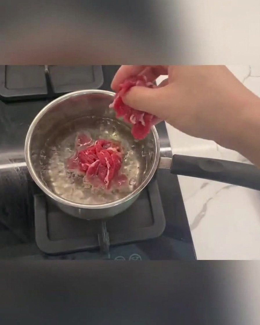 Beef slices cooking in boiling water with foam rising to the top.