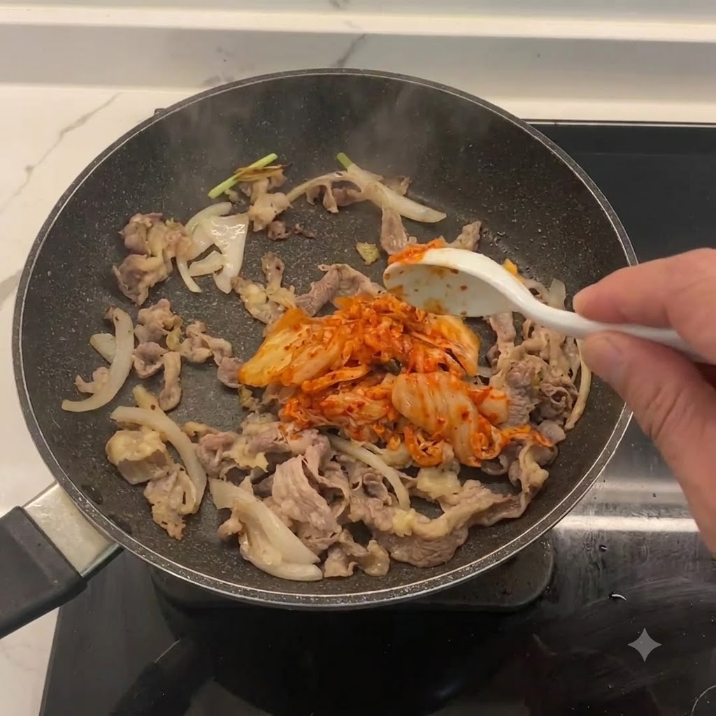 Chopped kimchi being mixed into the pan with beef and onions.