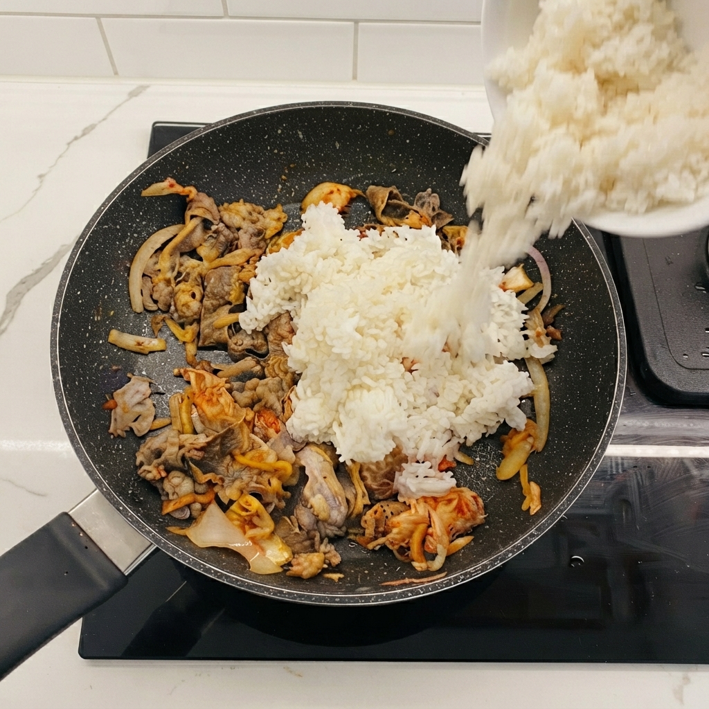 White rice being poured from a bowl into the frying pan containing beef and kimchi.